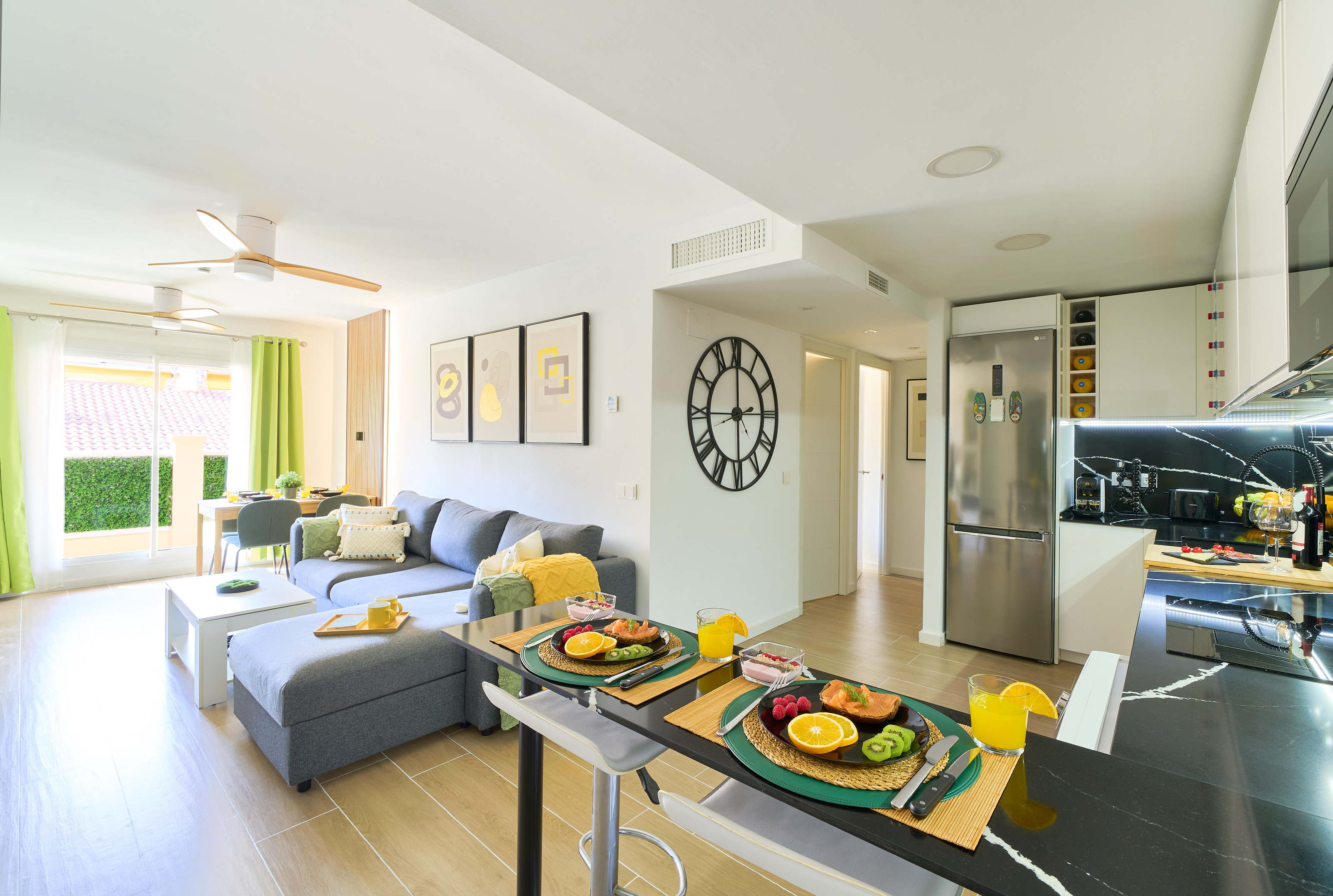 Stylish open-plan living room with a modern kitchen, smart TV, and natural light throughout — ideal for relaxing or sharing a glass of wine after a day by the beach.