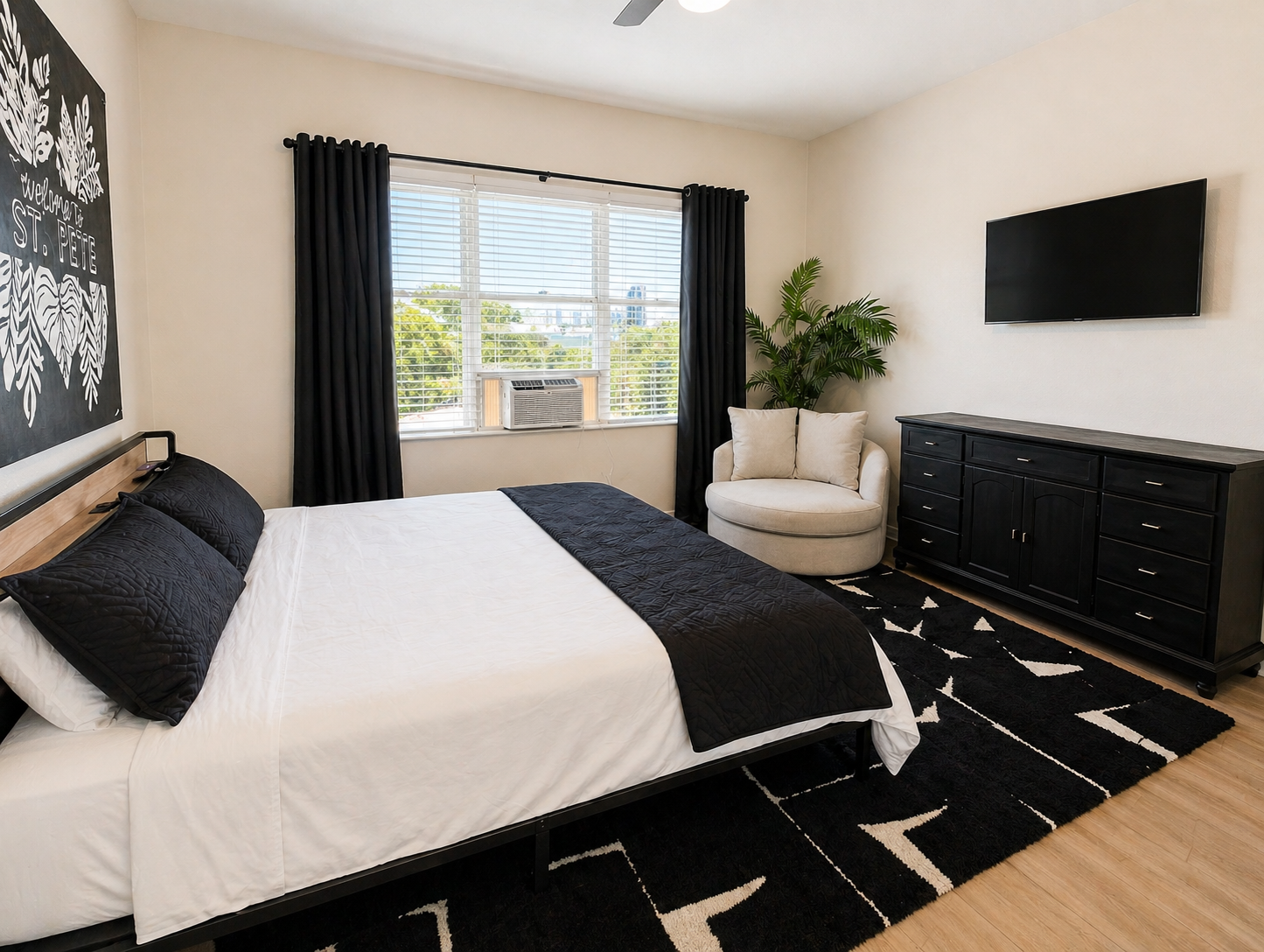 Stylish and cozy bedroom featuring a comfortable queen bed, soft linens, and modern décor. Enjoy natural light, a wall-mounted TV, and a relaxing reading chair—perfect for unwinding after a long day.