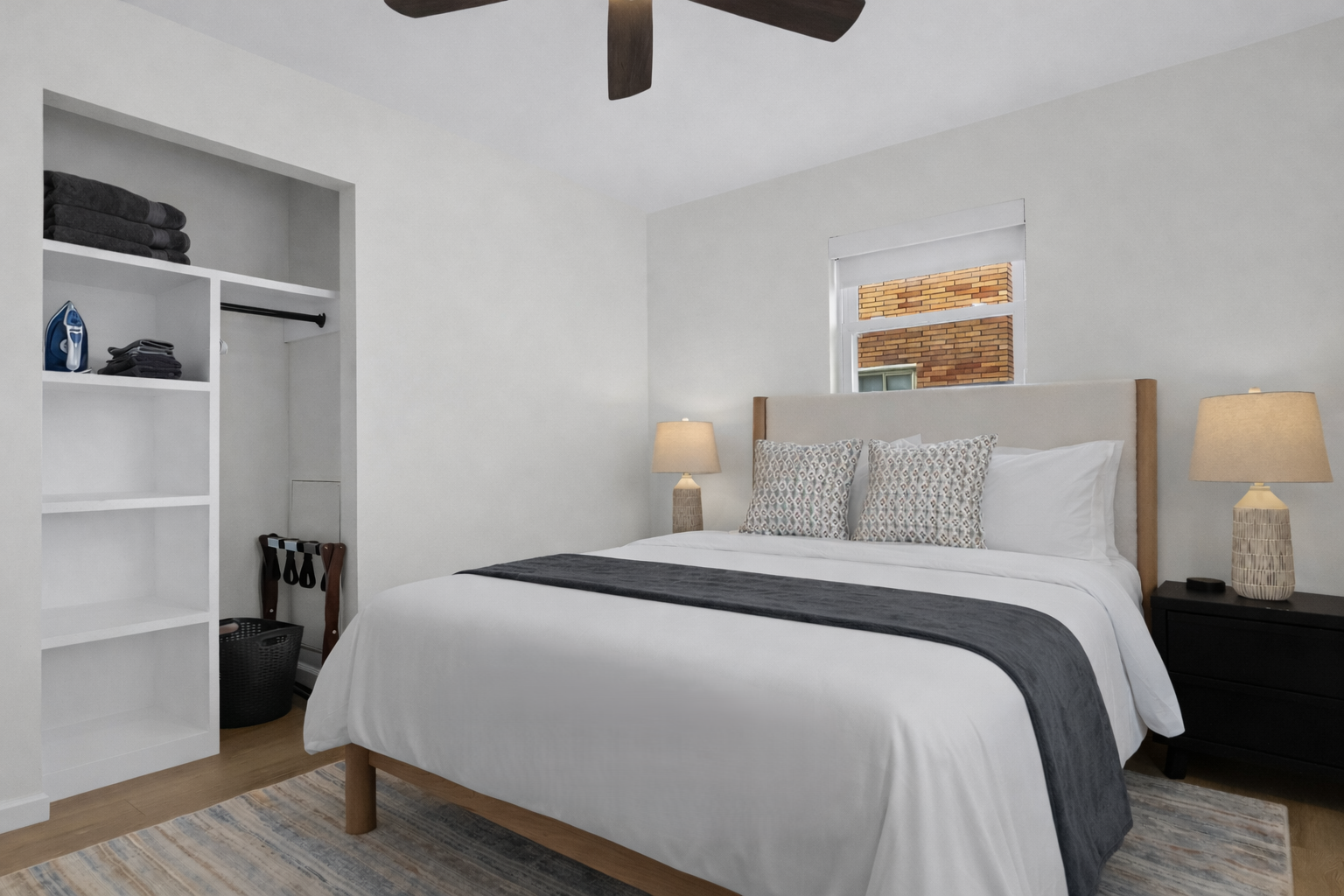 Rest easy in this bright bedroom with a cozy bed, soft linens, ceiling fan, and open closet storage—simple, comfortable, and thoughtfully designed.