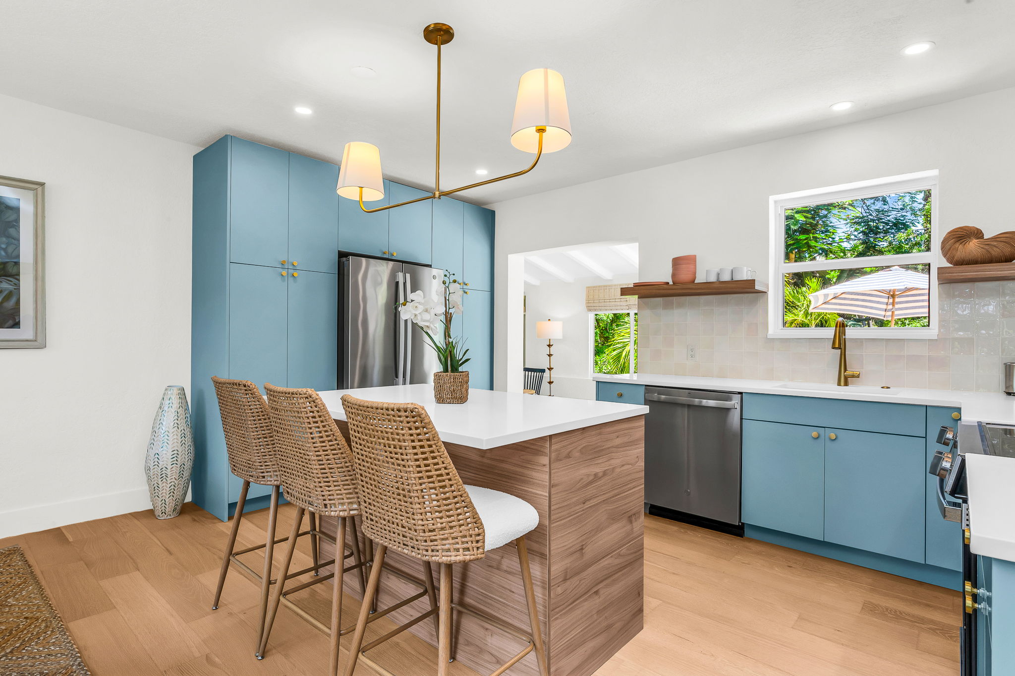 Gourmet kitchen with sleek quartz countertops, custom blue cabinetry, brass accents, and high-end stainless steel appliances. Features an oversized island with seating, open shelving, and designer lighting—perfect for both cooking and entertaining in style