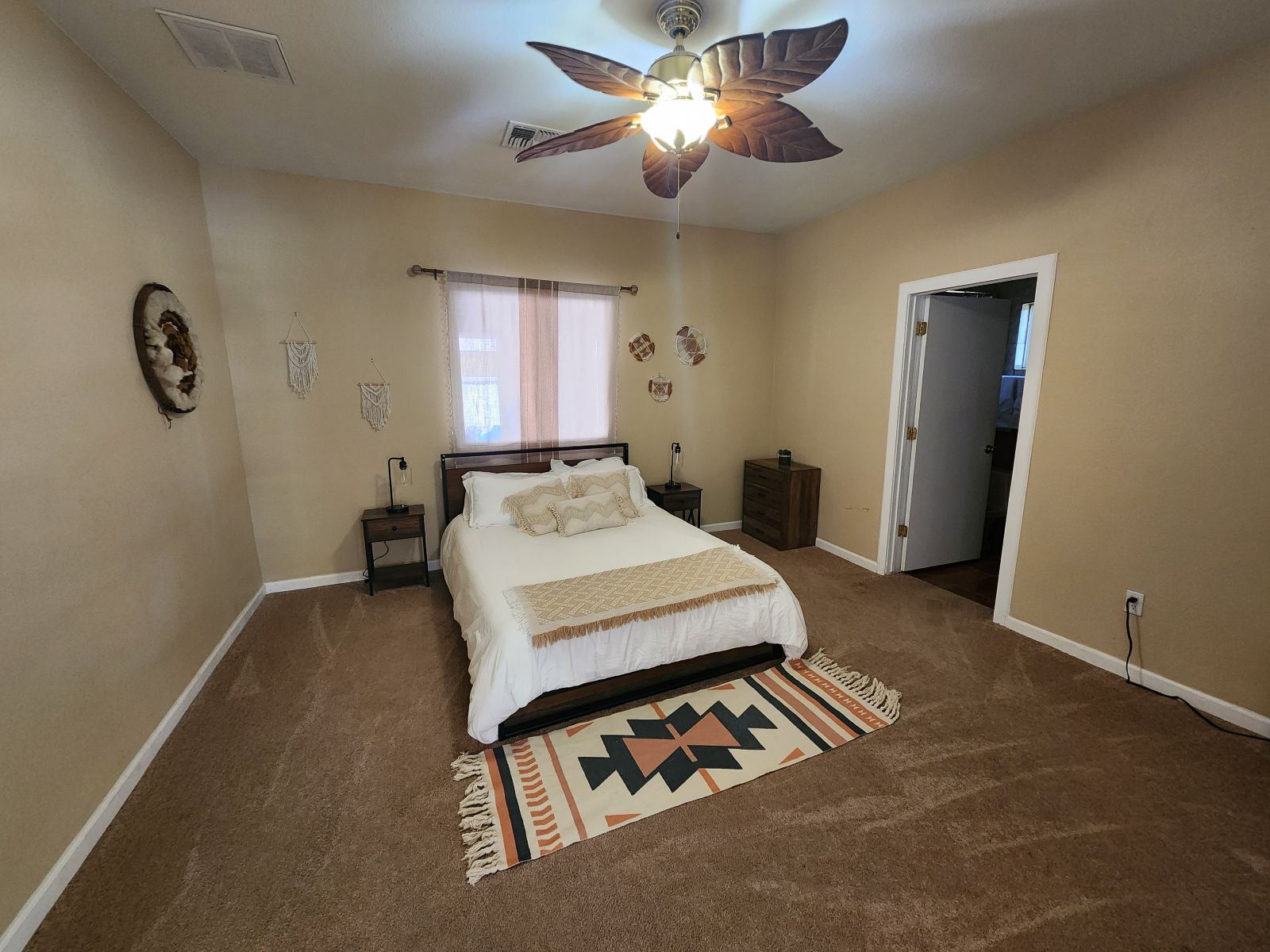 This spacious bedroom offers a peaceful desert-inspired retreat, complete with cozy linens, tribal accents, and a tropical ceiling fan for added charm.