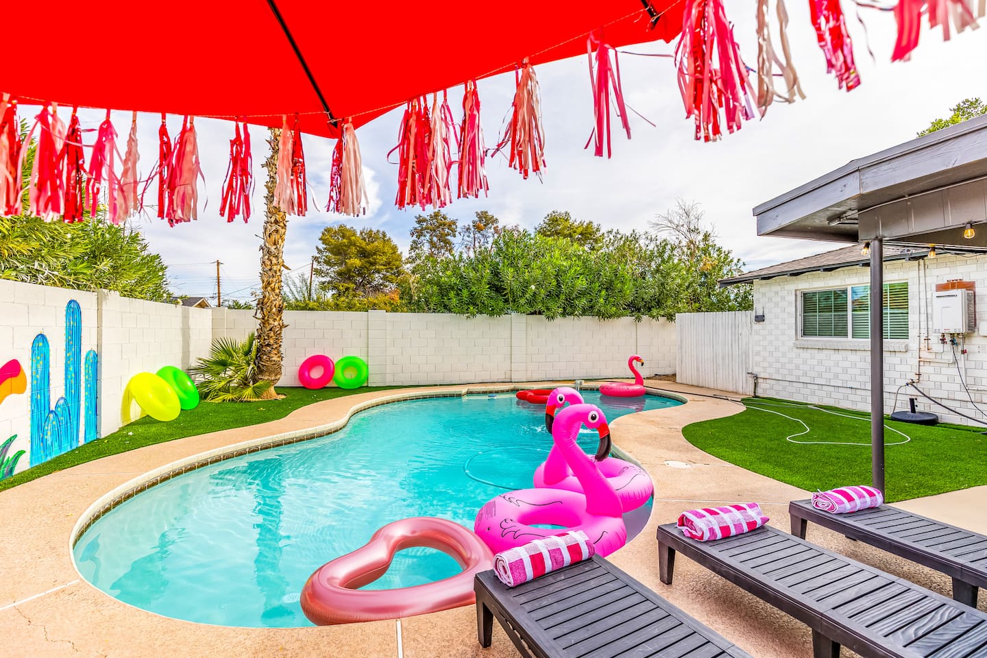 Relax poolside beneath a vibrant red umbrella with fun fringe tassels, while colorful floaties add a playful touch to your Scottsdale retreat.

