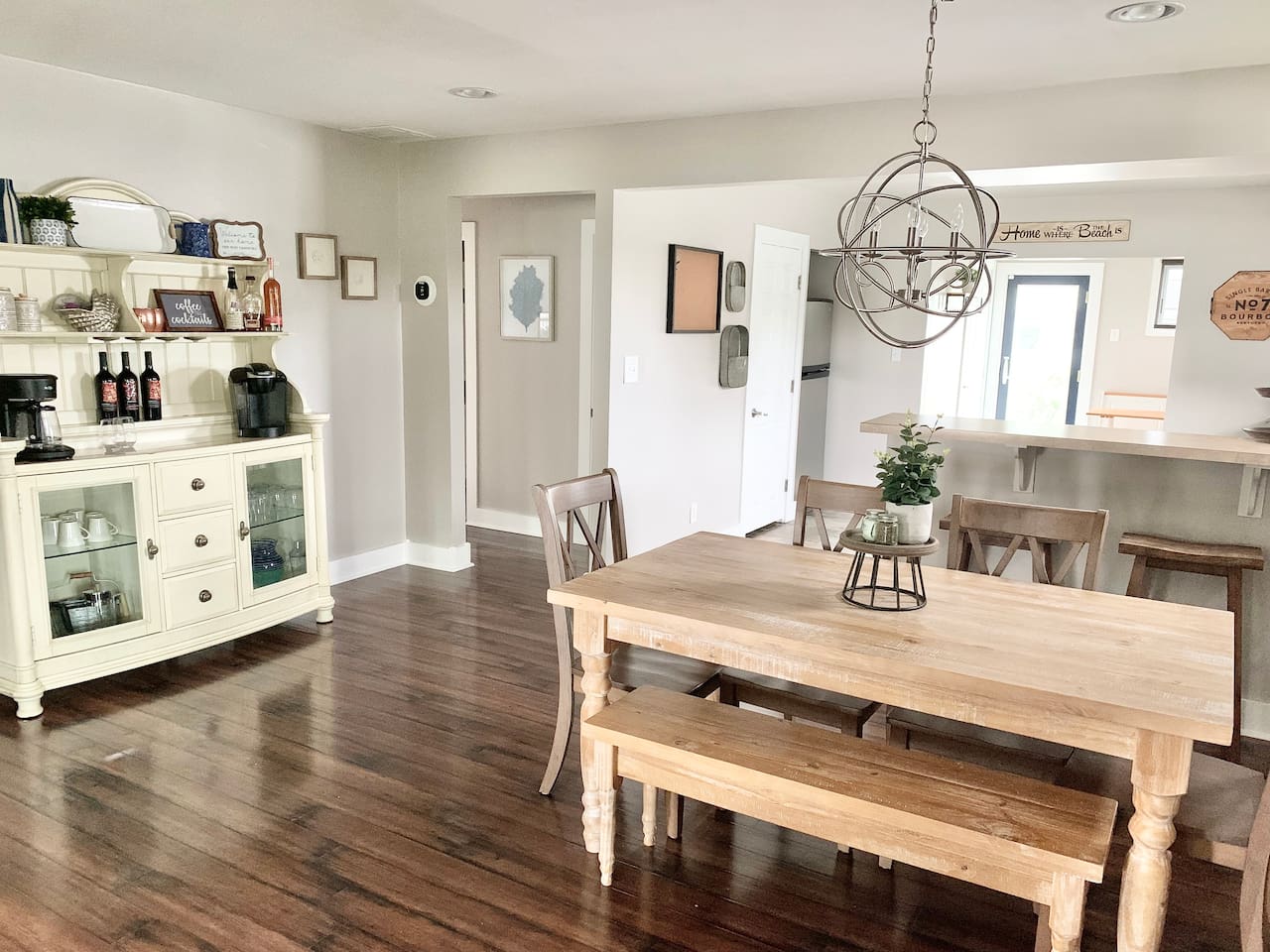This charming dining area features a farmhouse table with bench seating and a unique orbital chandelier. A white hutch serves as a coffee and wine station, making it easy to enjoy a beverage before heading to the shore.