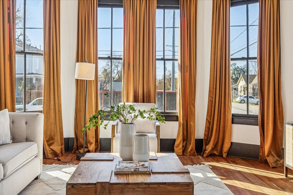 Towering windows flood the living room with fabulous natural light, highlighting original hardwood floors reinforcing the home’s unapologetic blend of historic grit and modern attitude.