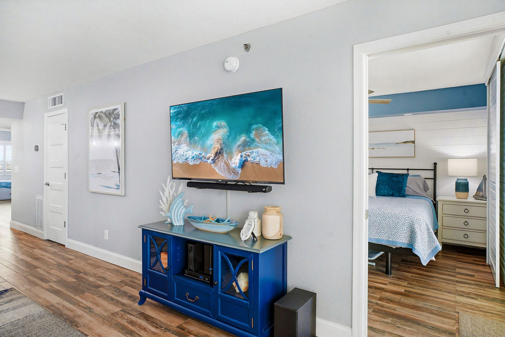 Bright living area with smart TV, stylish beach décor, wood flooring, and easy access to a comfortable private bedroom, creating a relaxing open-concept retreat.