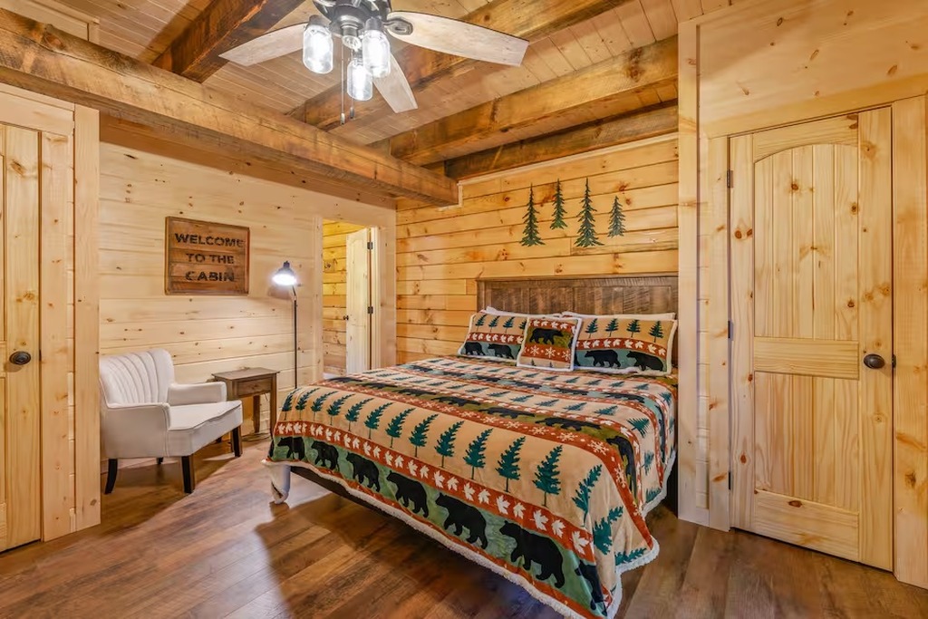 Unwind in the king bedroom at Bear Paws Cabin after a full day of Smoky Mountain adventures. A wall-mounted Smart TV, ensuite bathroom, and rustic cabin d&eacute;cor give parents their own comfortable space in this 2-bedroom Gatlinburg family cabin rental.