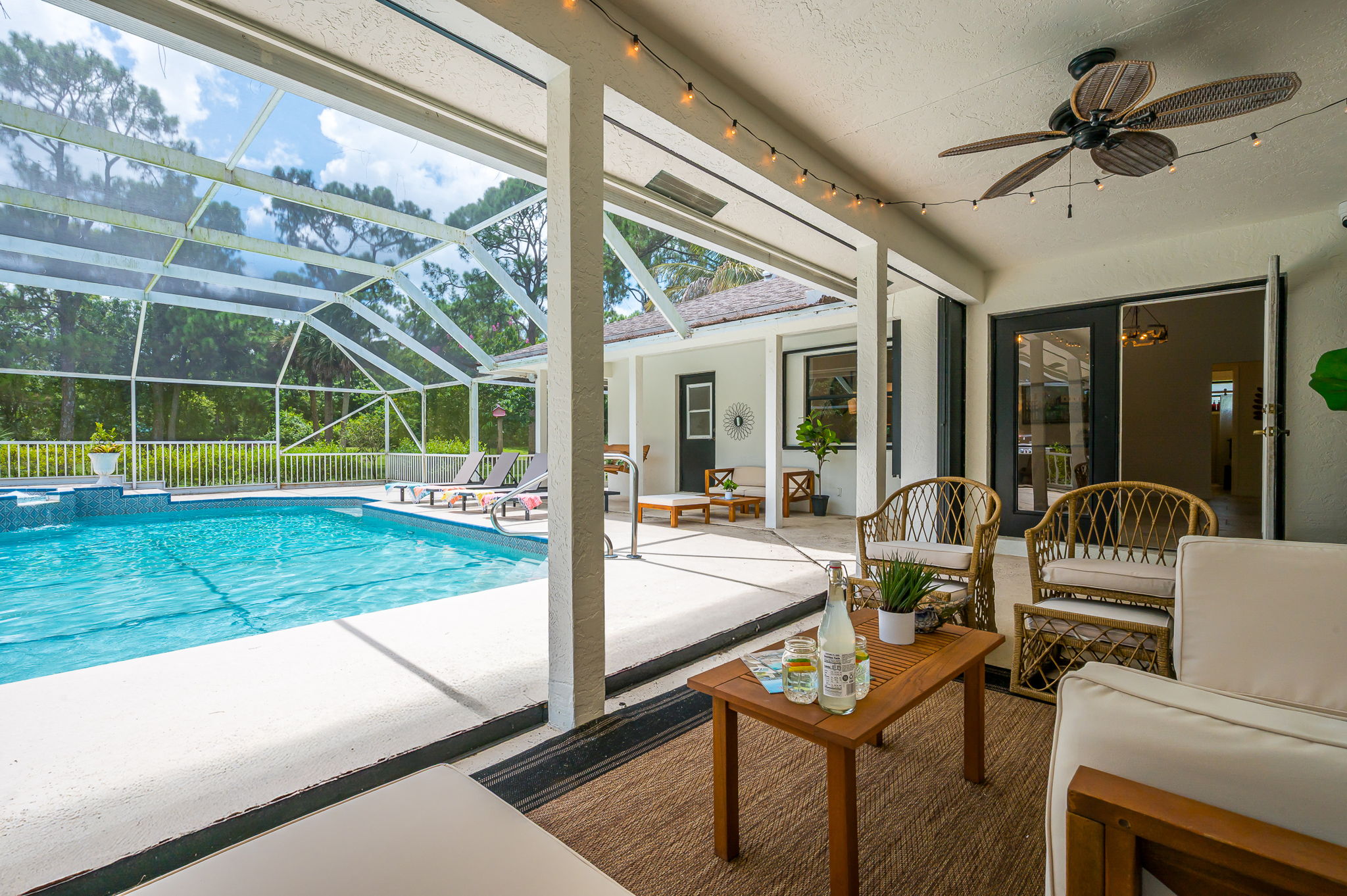 Screened-in pool area with heated pool and spa, surrounded by lush greenery. Features ample lounge seating, BBQ grill, and cozy covered patio with outdoor dining and relaxing sitting area.