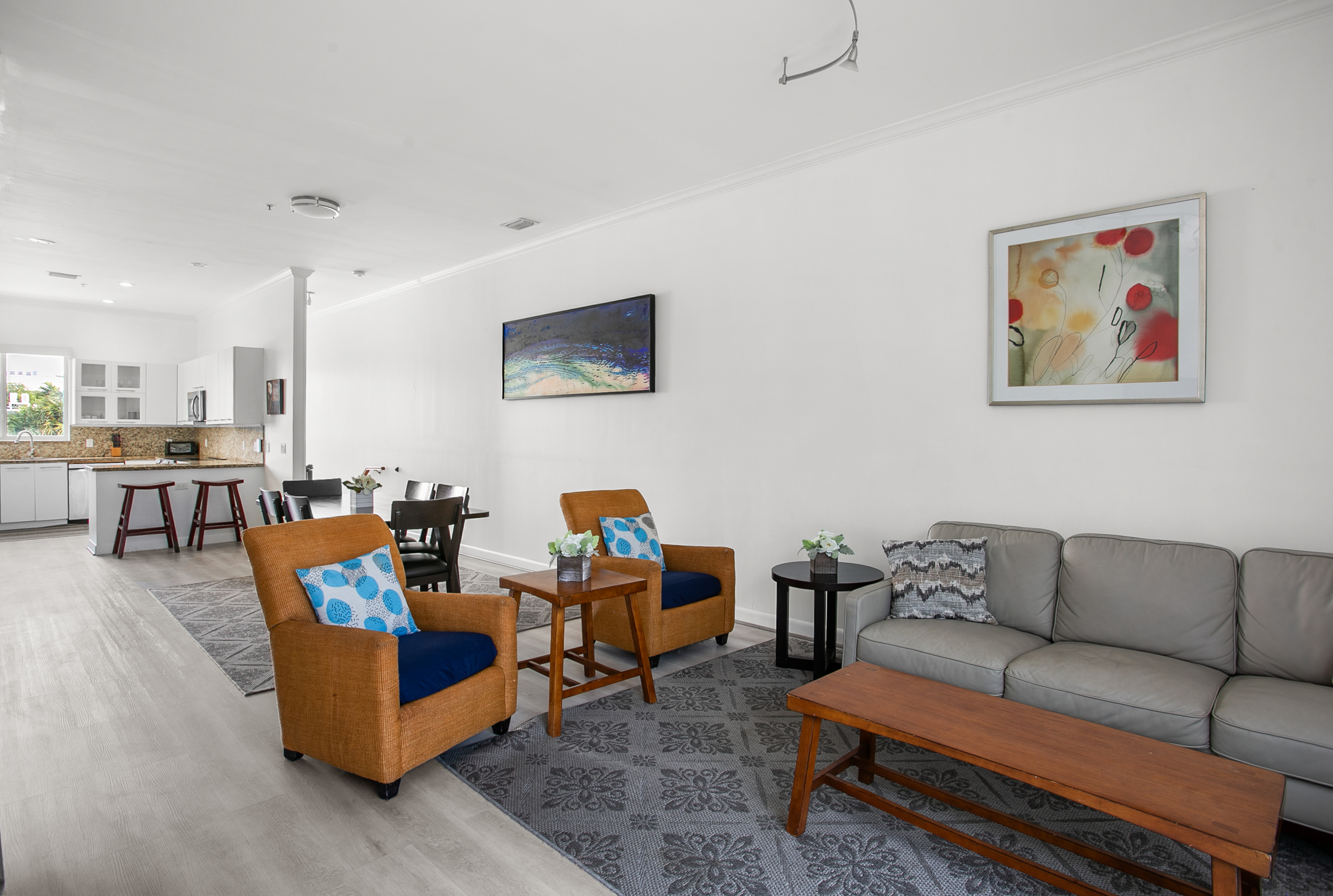Living room with leather sofa, accent chairs, and a 50-inch flat screen TV. Sliding glass doors open to a Juliet balcony for sea breeze.