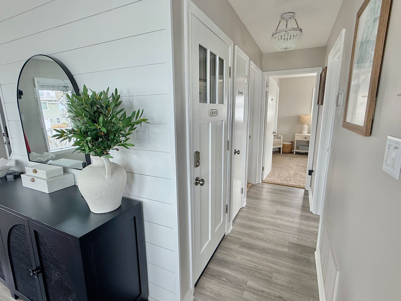 You are welcomed by a bright and charming hallway, featuring crisp white shiplap walls and an elegant black console table that sets a stylish tone for the rest of this inviting coastal home.