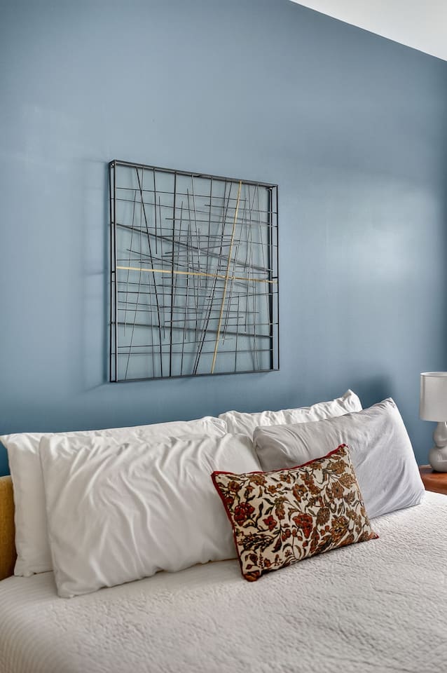 Wake up surrounded by modern design. This bedroom blends soft white linens, a calming blue accent wall, and artistic décor—an oasis of style and tranquility in the heart of the city.