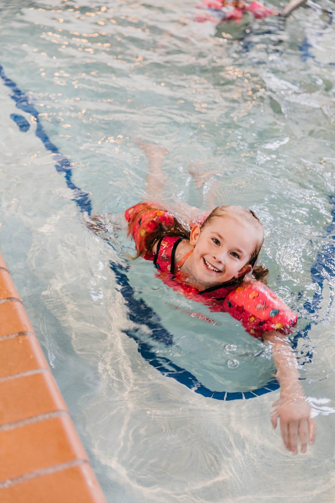 A smiling girl in a swim vest swimming in the indoor pool at the Waterfront Plaza building in Canal Park