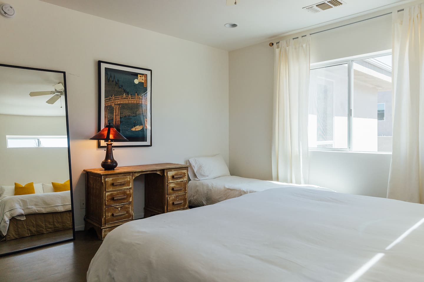 Well lit bedroom has full length mirror and extra small bed.