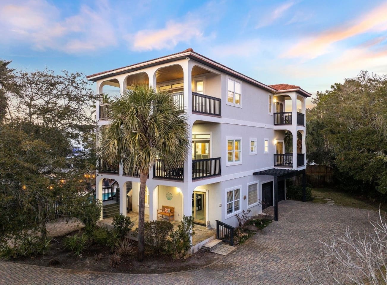 Welcome to The Copper Fin! Grand front view highlighting custom arched balconies, extensive paver parking, and a lush coastal setting.
