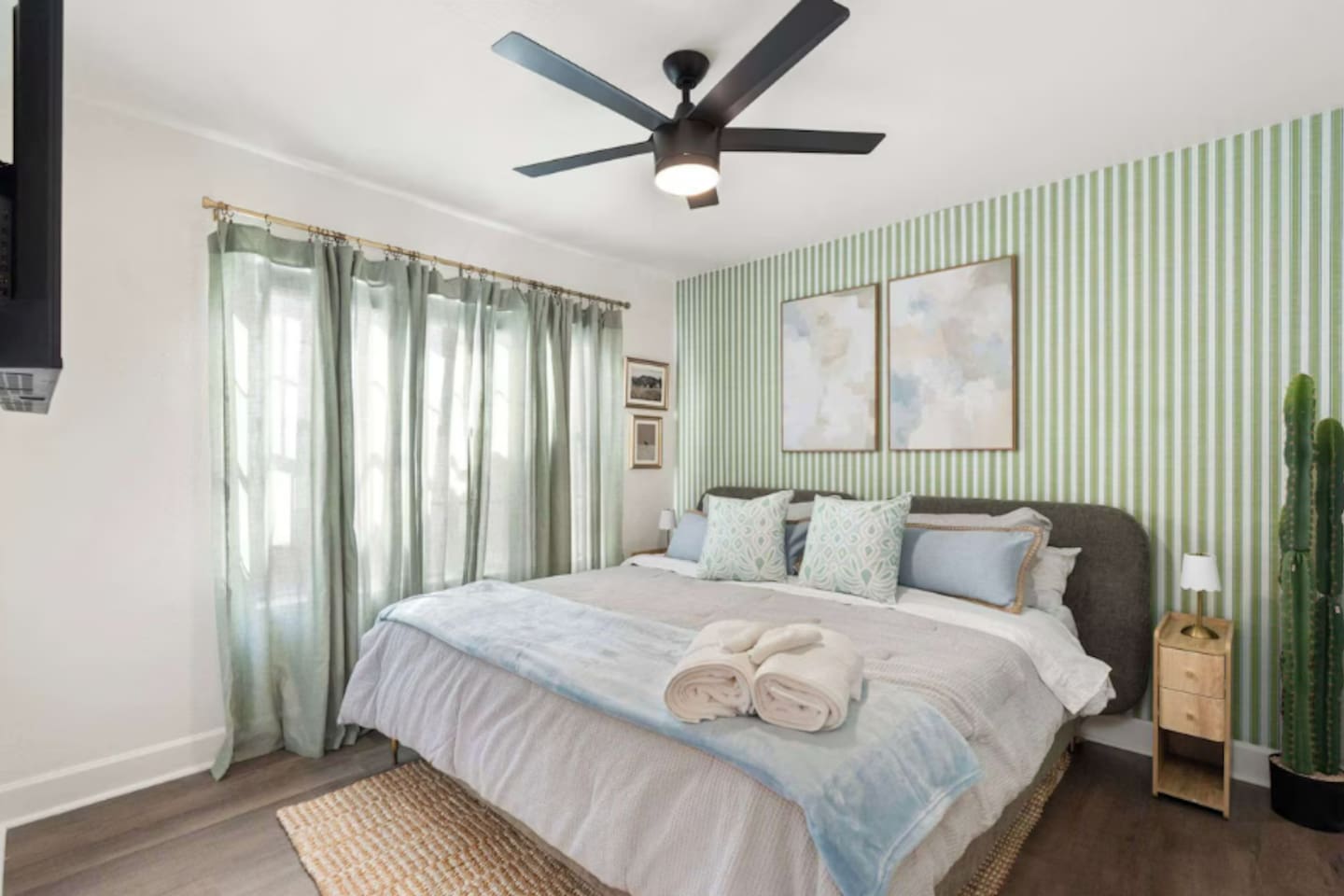 Bright guest bedroom with green striped accent wall, soft linens, and natural light—a calming retreat with thoughtful style.