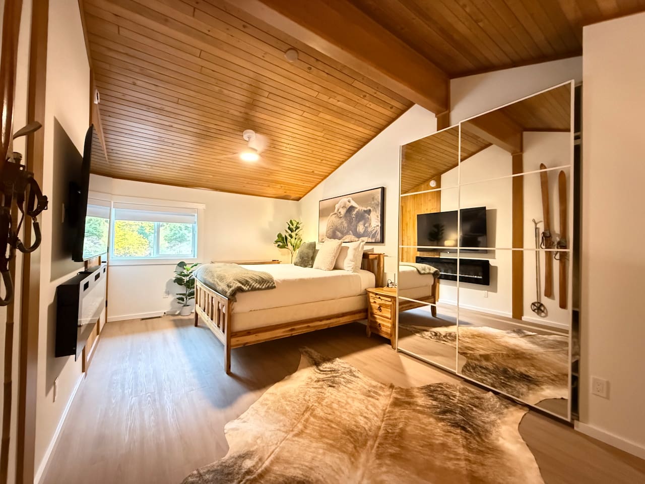 Primary Bedroom Loft Suite: A spacious loft bedroom featuring a comfortable queen-size bed, a modern built-in electric fireplace, a 65" Smart TV, closet with mirrored doors and dresser storage solutions for your gear.