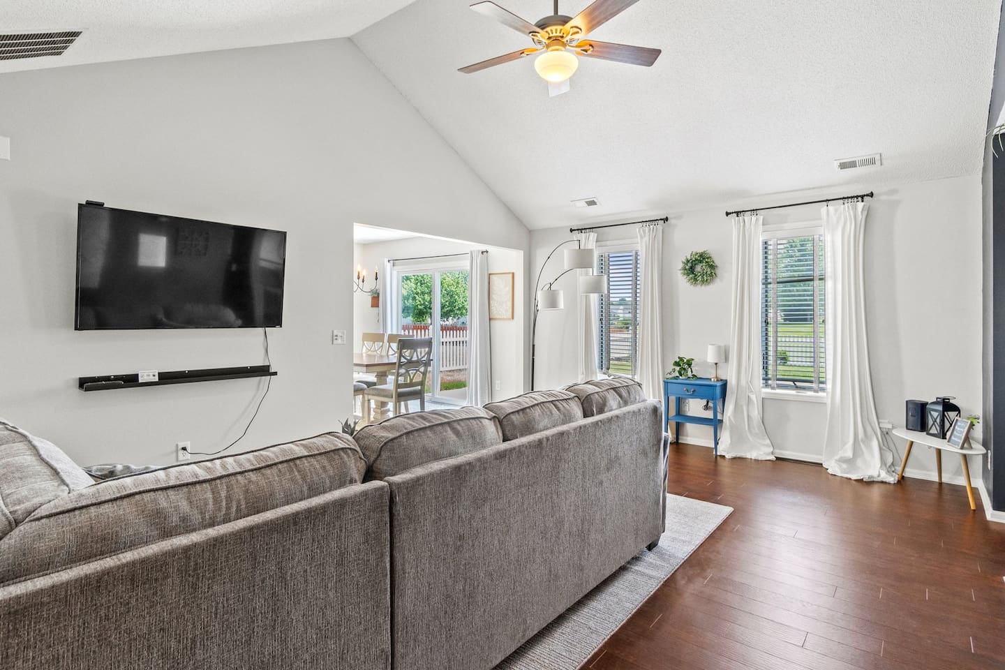 Natural light pours through large windows, highlighting the neutral color palette, modern furniture, and mounted smart TV — perfect for movie nights.

