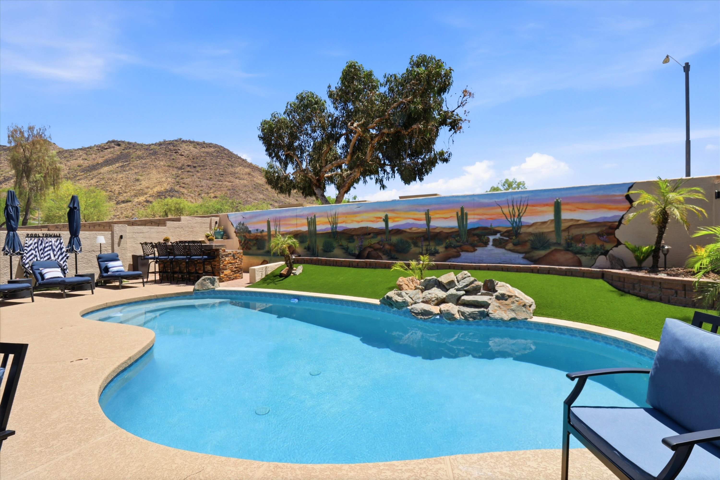 Private backyard pool with lounge seating, desert mural, mountain views, and open space for sunny outdoor relaxation.