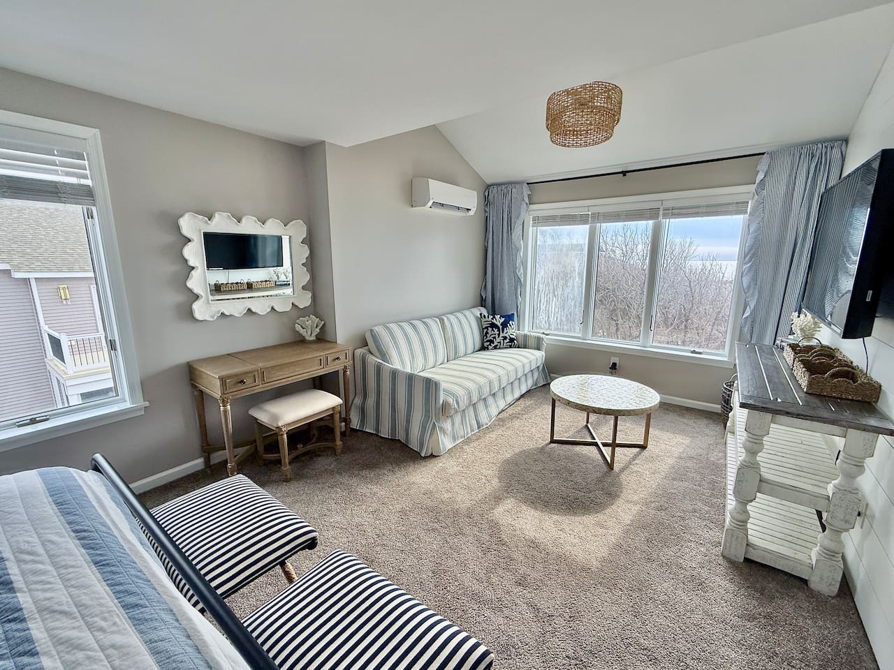 The master bedroom features this bright, versatile living space features a cozy striped sofa, a wooden vanity with a decorative mirror, and scenic windows, creating a perfect, light-filled retreat for guests to relax during their stay.