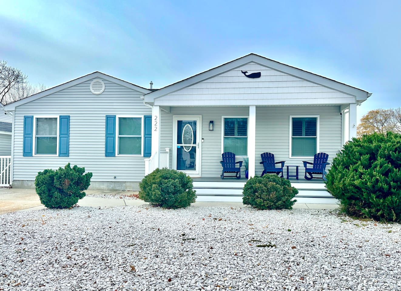 Welcome to this charming coastal home featuring light blue siding and vibrant blue shutters. The front porch is perfectly set up for relaxing with classic Adirondack chairs and a whale accent above the entryway.
