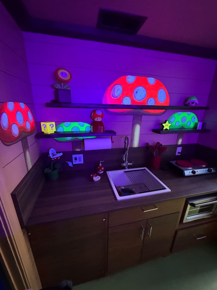 Step into the magical Toadstool Cafe-inspired kitchen! Giant Super Mario mushrooms GLOW IN THE DARK on floating shelves, and a full sink/counter setup in the modern compact kitchen create a fun, colorful space for family cooking and snacks.
