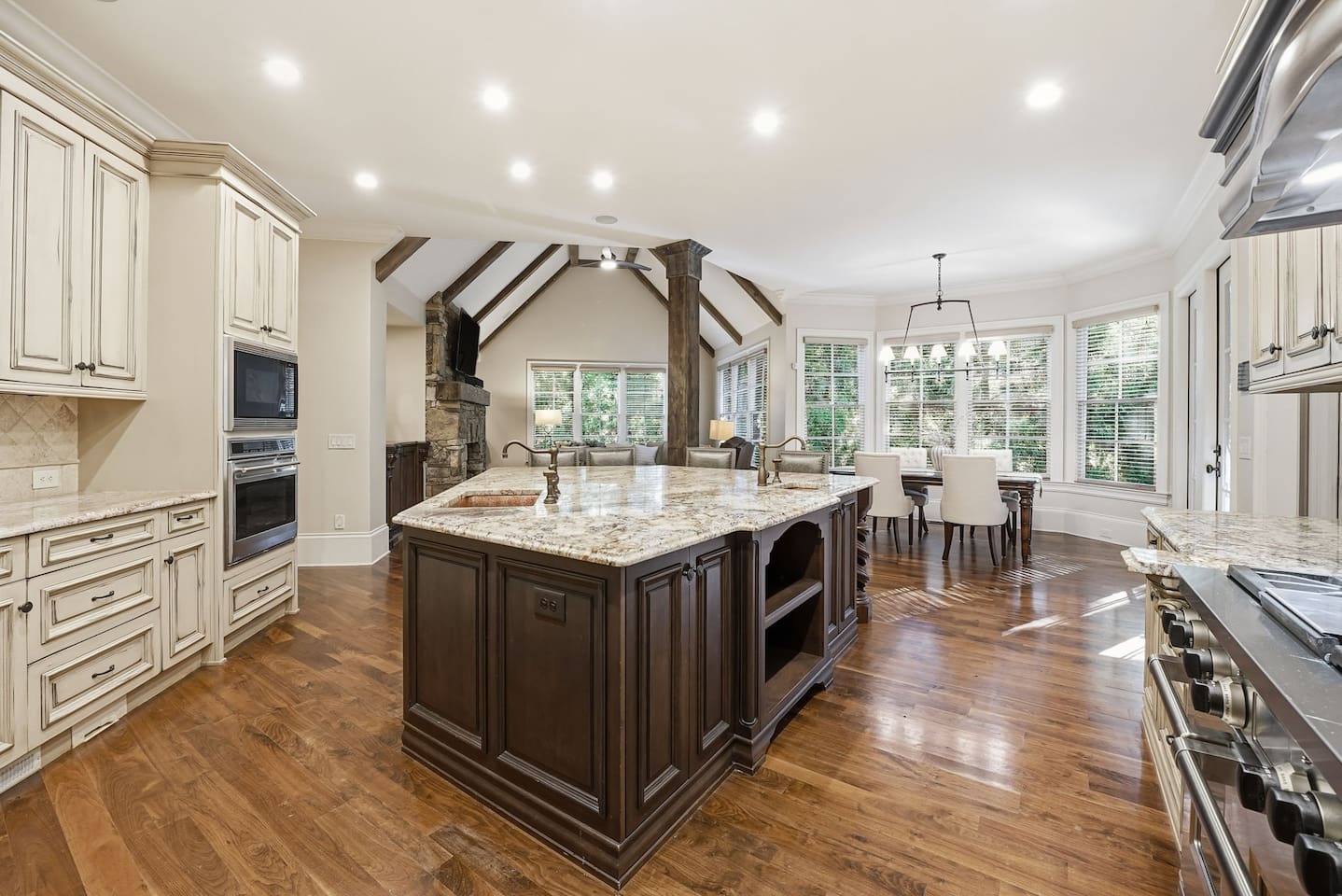 This open kitchen features beautiful cream wood cabinetry, sleek granite countertops, and an island that comfortably seats four. The bright, airy design makes it the perfect place to cook, gather, and share meals together.