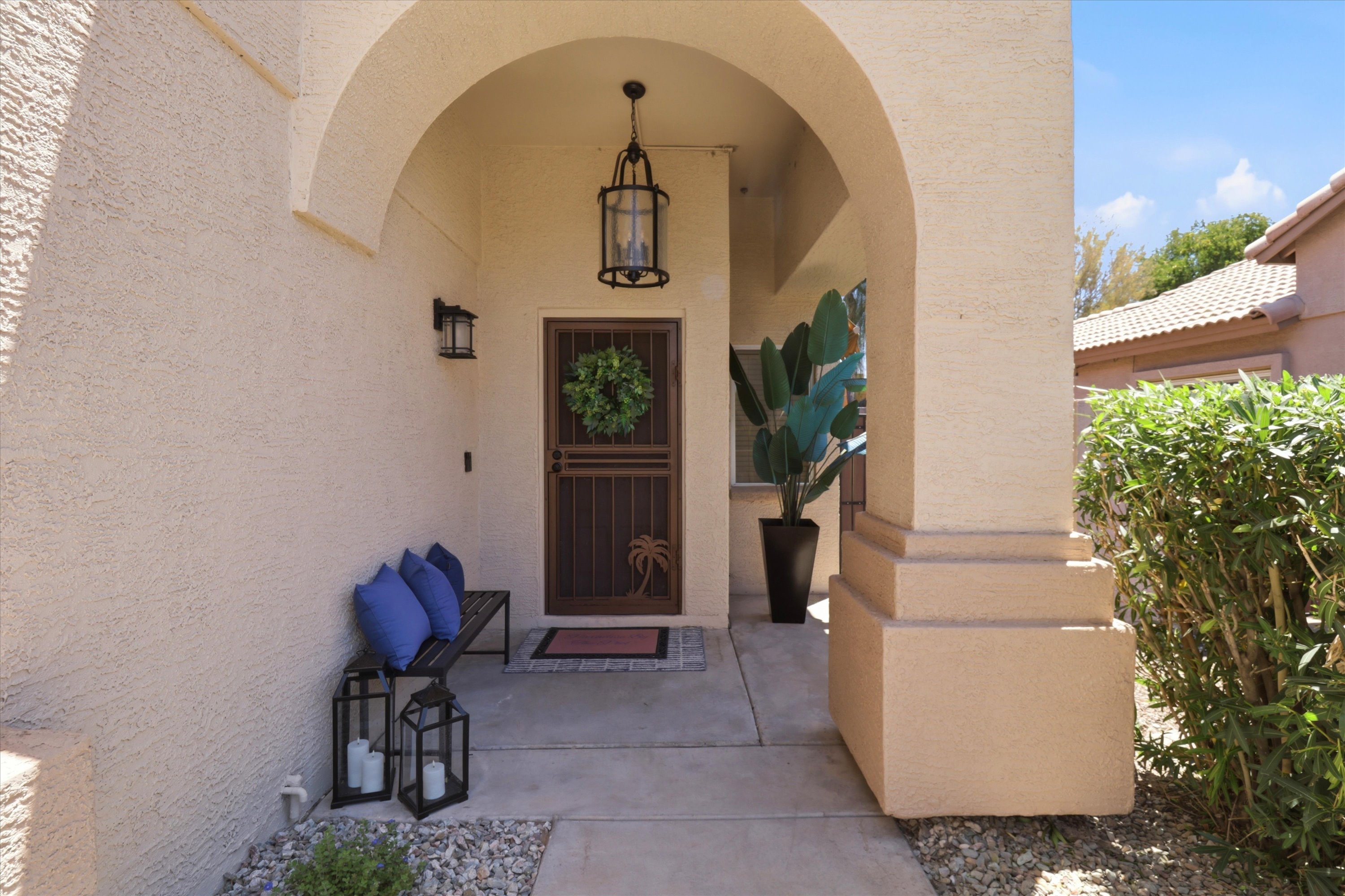 Covered entry with arched detail, bench seating, and a shaded arrival path to the home.