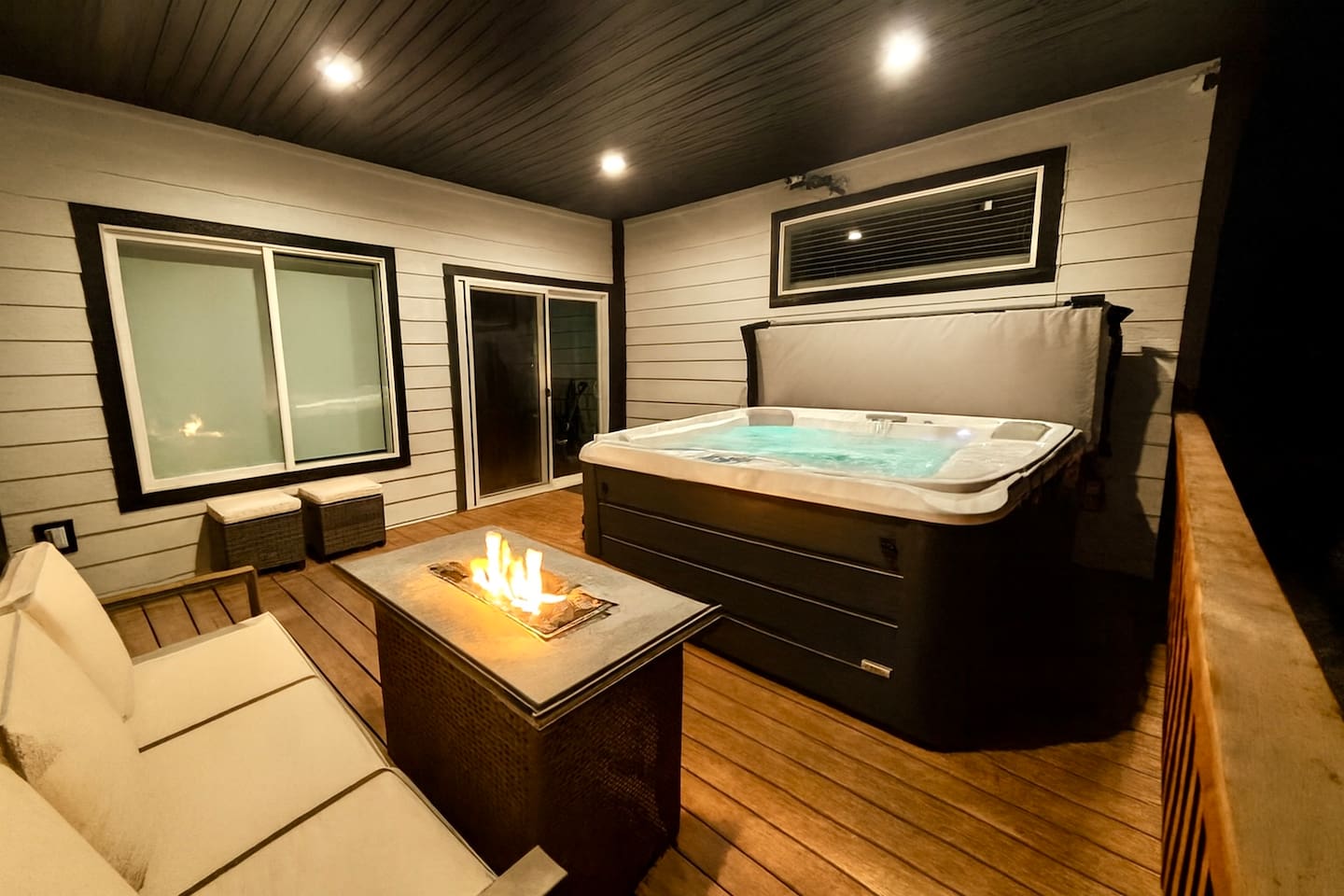 Unwind in this cozy forest-side patio featuring a bubbling hot tub, crackling fire pit, and plush seating—all under a warm, well-lit canopy. Perfect for snowy escapes, stargazing, and serene mornings with nature.

