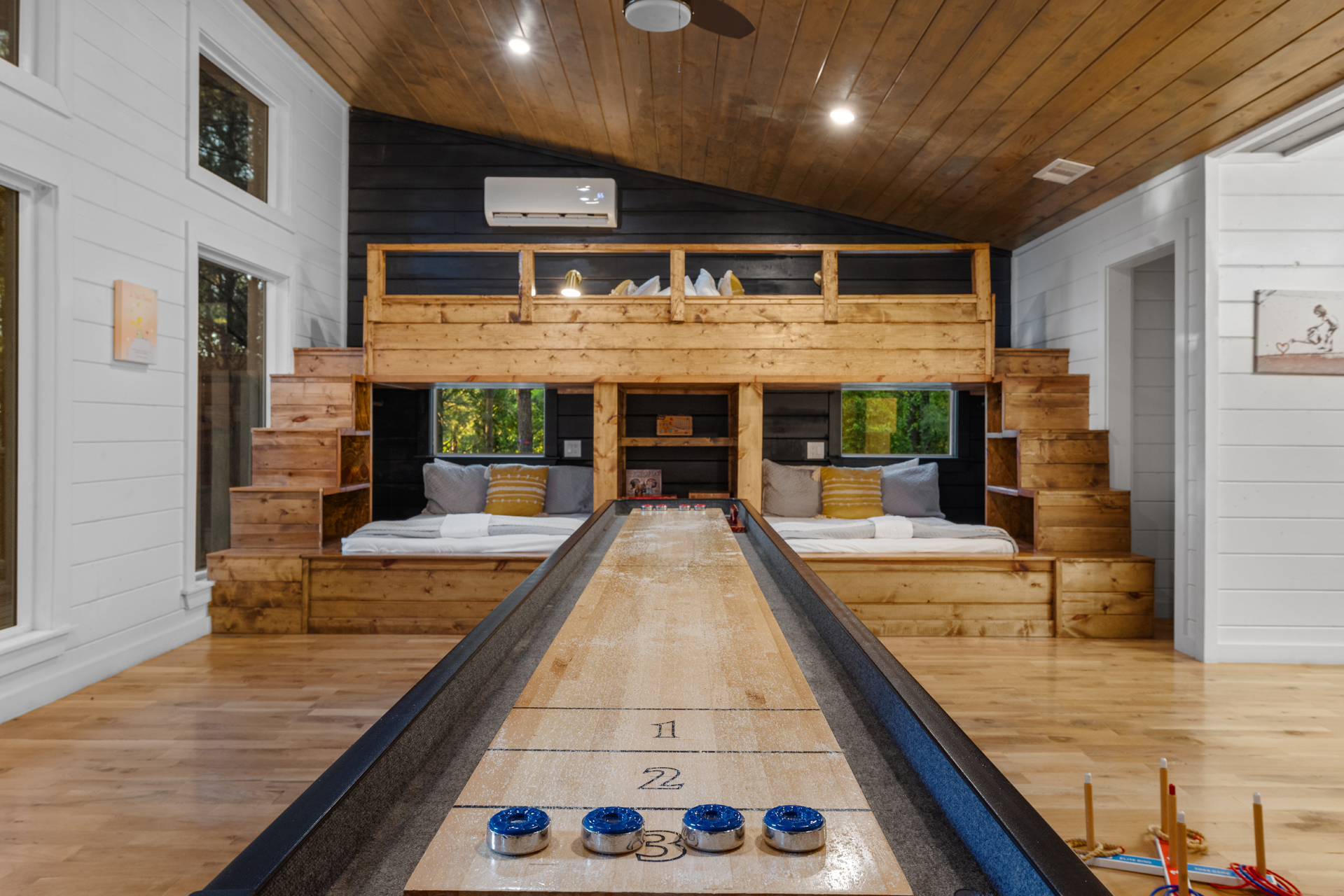 A fun bunk room made for groups — featuring twin beds with a connected upper bunk, side stairs, and lower bunks for extra sleeping space. A central game area with board games makes it perfect for bonding and fun nights in. 🎲