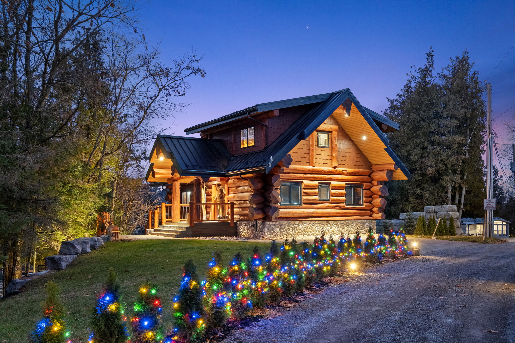 Charming log cabin at dusk with festive landscape lighting and a peaceful wooded backdrop—perfect for a relaxing getaway.