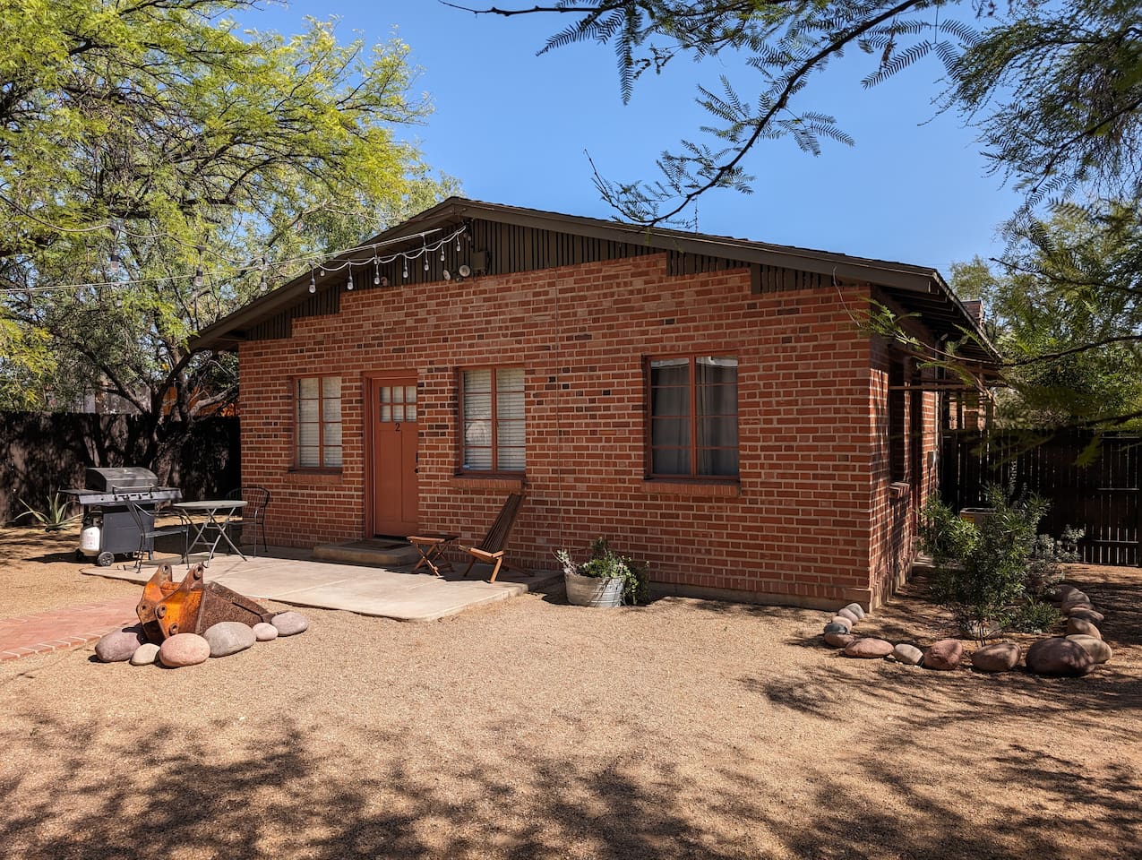 Entrance in a large shared backyard with patio, gas grill, and backhoe bucket fire pit.