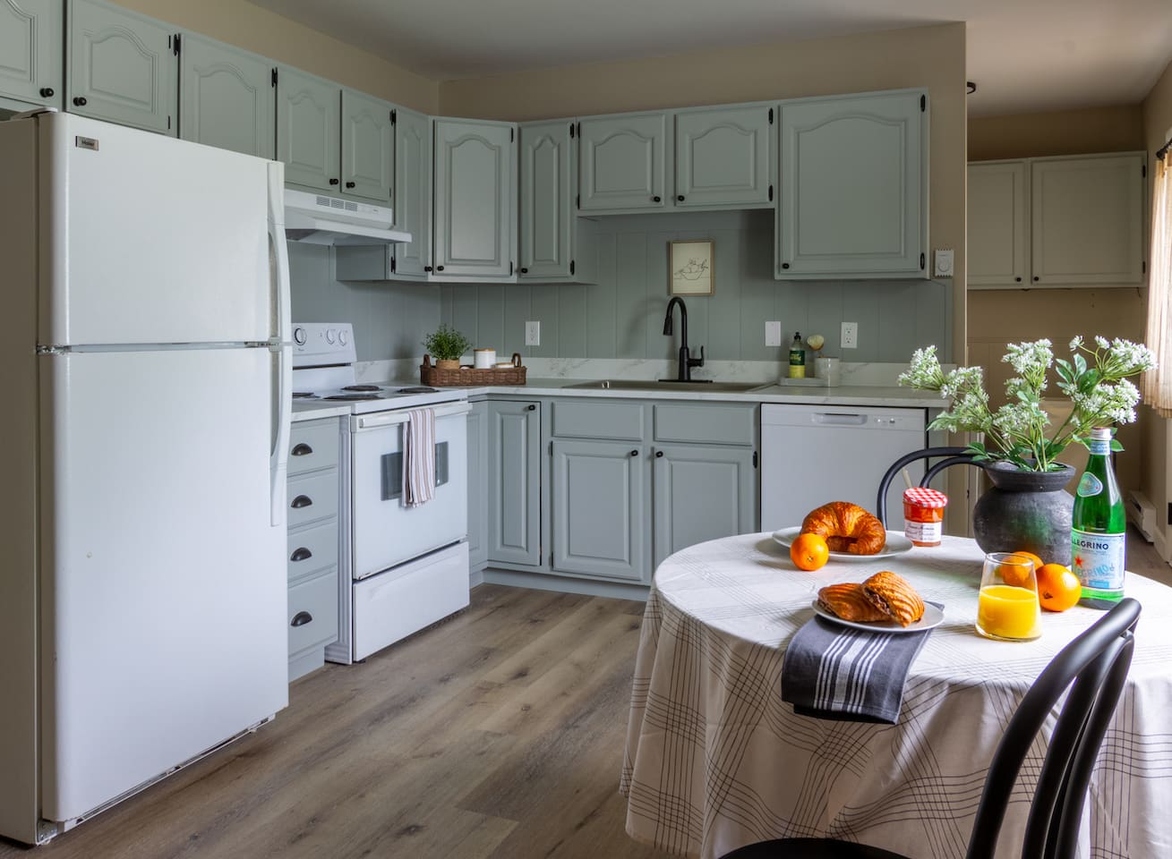 Sage cabinetry and classic finishes give the kitchen a cheerful, homey character.