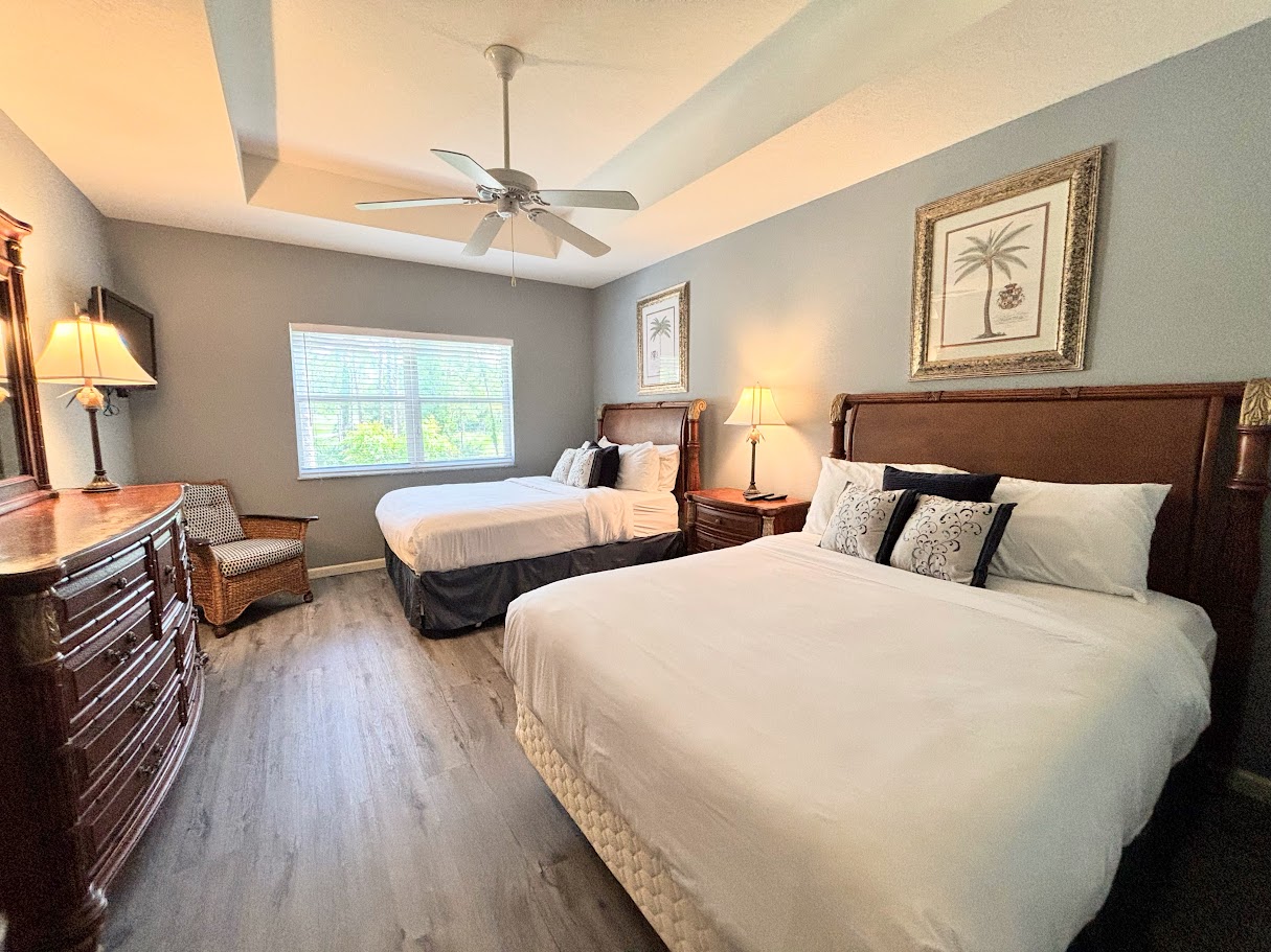 Comfortable bedroom featuring two beds, ceiling fan, dresser storage, and warm natural light.