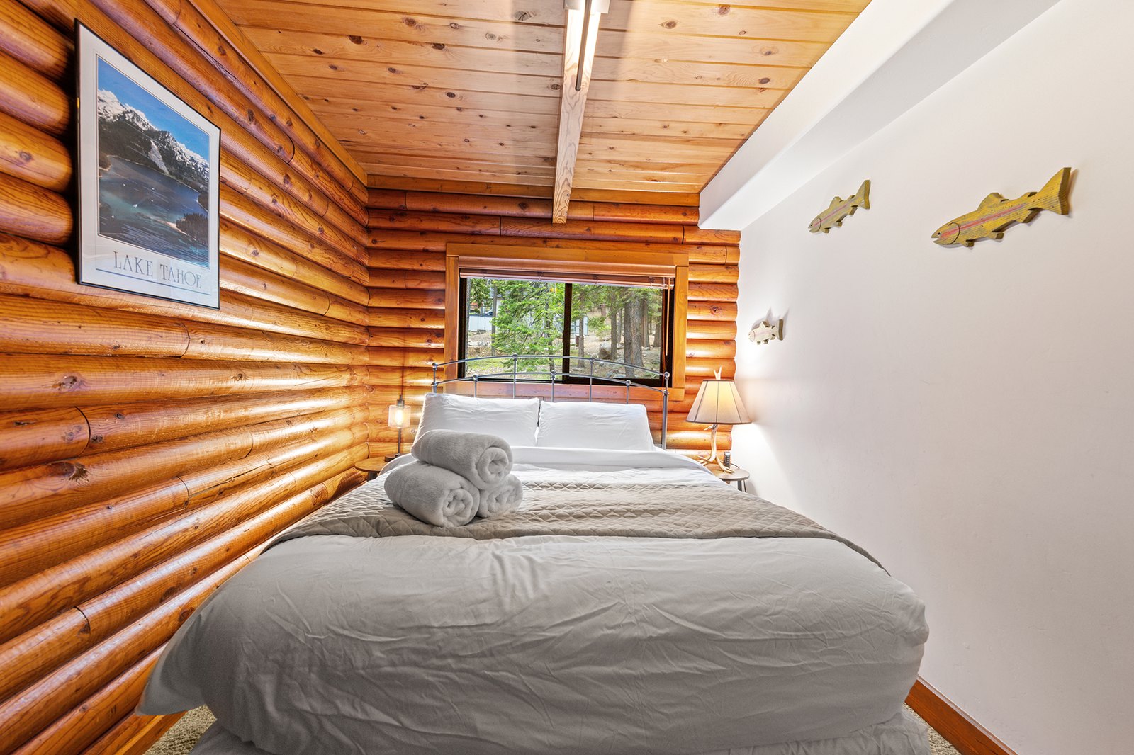 Sleep inside the real thing — solid log walls, a vintage Tahoe print, and the forest right outside the glass.