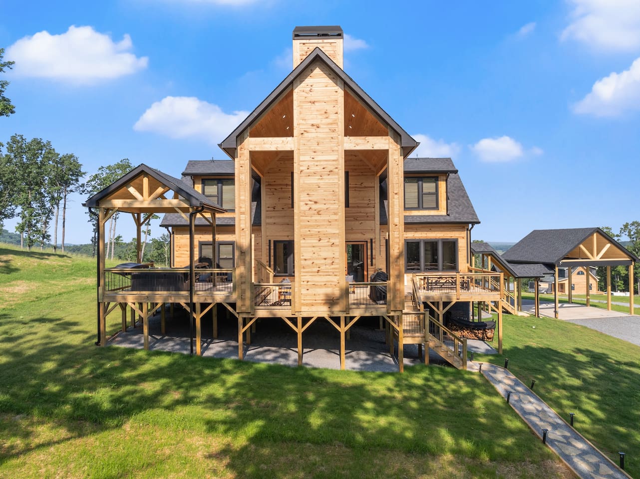 Framed by twin staircases and a towering chimney, this dramatic rear view showcases the elevated deck with a covered hot tub area—perfect for unforgettable mountain evenings.