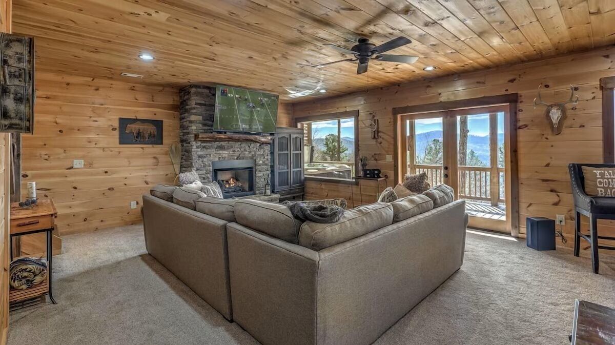 Spacious downstairs lounge featuring a stone fireplace, large TV, and comfortable seating for gathering after a day in the mountains.