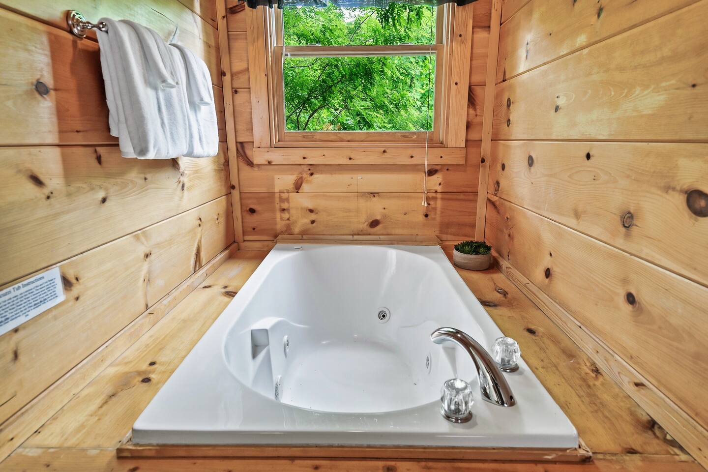 A luxurious jetted tub nestled within warm wood-paneled walls is perfectly positioned beneath a window, offering a peaceful soak with views of lush greenery outside.