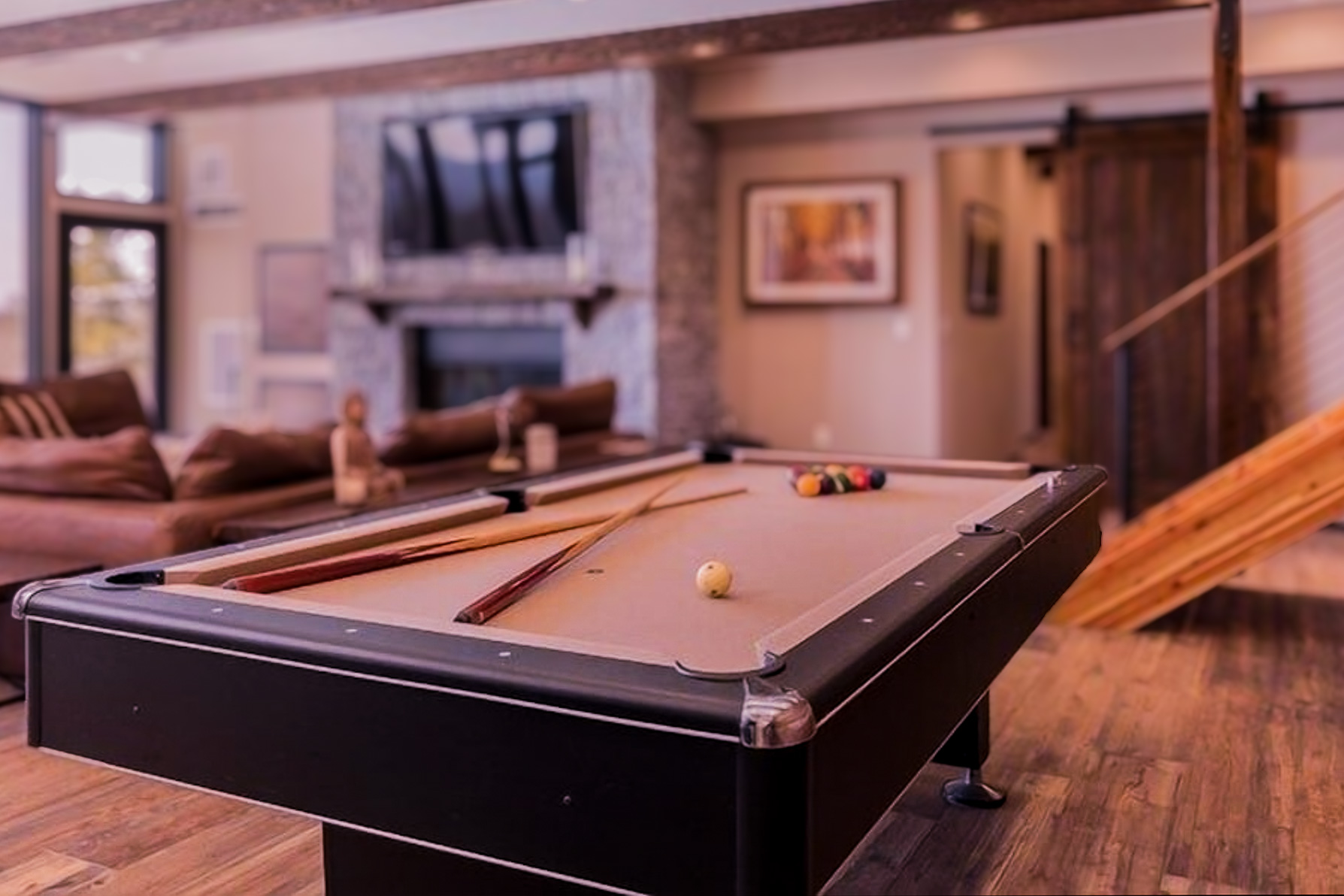 The Tavern Room at Sunset Falls &mdash; pool table foreground, stone fireplace and 85 inch TV background, leather sectional, beam ceiling