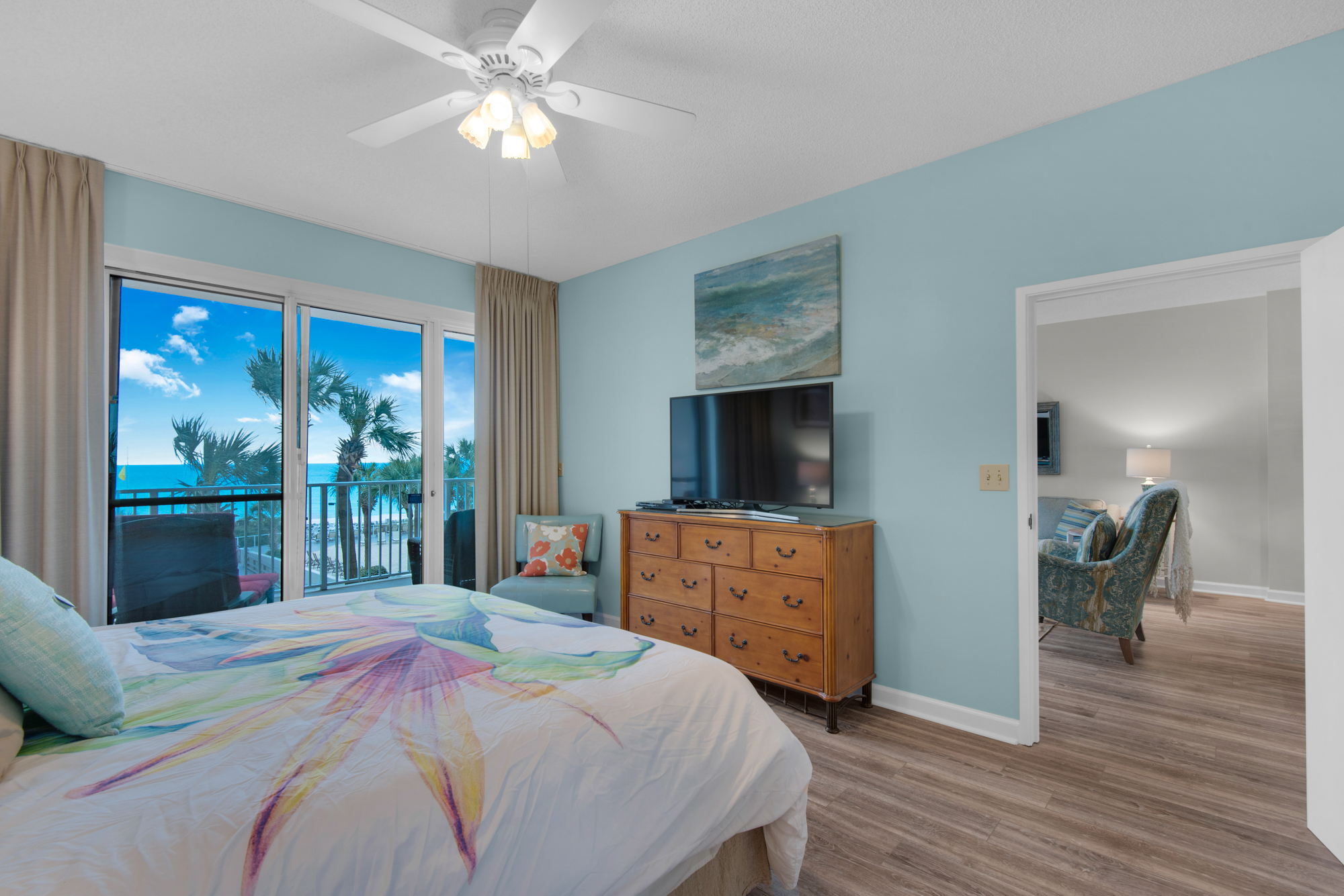 Primary king bedroom with Gulf views, balcony access, and a TV. Living-room furniture visible in the adjoining room has since been replaced.