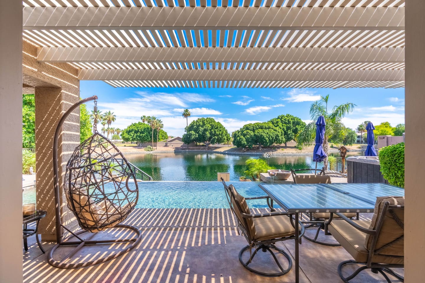 Dine under the pergola with the pool and lake as your backdrop — the hanging egg chair, lake breeze, and open sky make every meal out here feel like a vacation within a vacation.