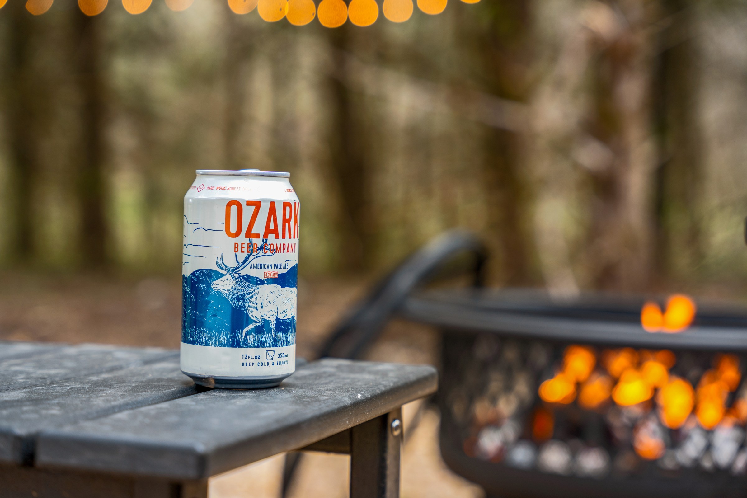 Fire pit glowing behind a local Ozark beer. String lights and a fire pit for the after-dinner hour.