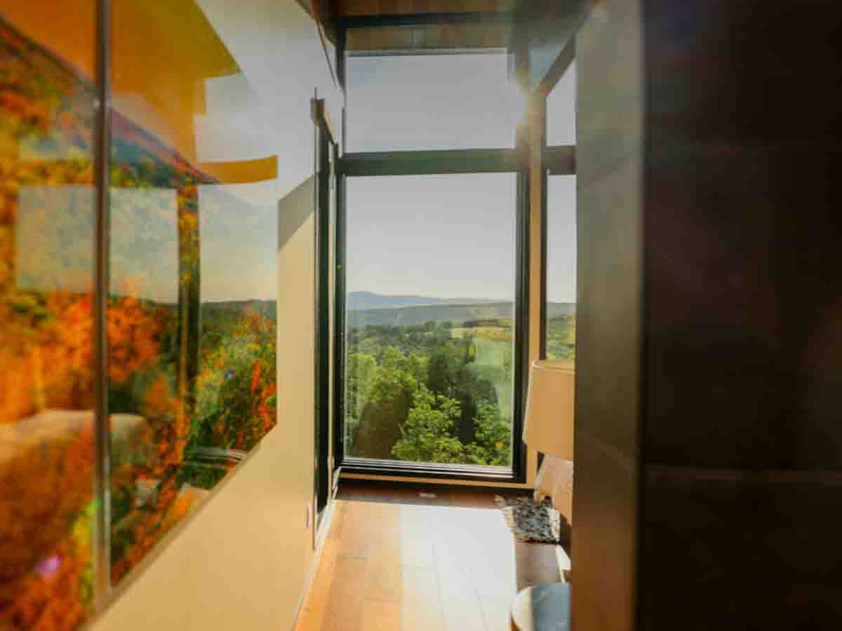 Primary Suite seating area looking through floor-to-ceiling glass to the green summer mountains &mdash; Sunset Falls Berkshires