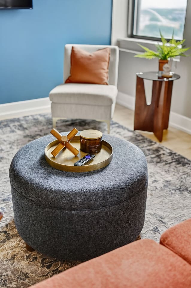 Unwind in a stylish living room featuring a modern accent chair, cozy ottoman with designer décor, and a calming blue wall. Perfect for relaxing with a glass of wine or streaming your favorite shows after exploring downtown Des Moines.