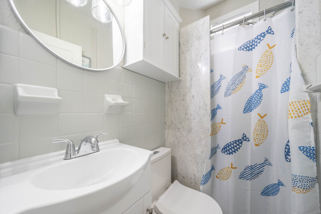 Clean, coastal-style bathroom with a walk-in shower, bright vanity, and ample storage. Fresh finishes, patterned shower curtain, and well-lit mirror make it easy to refresh after a beach day.