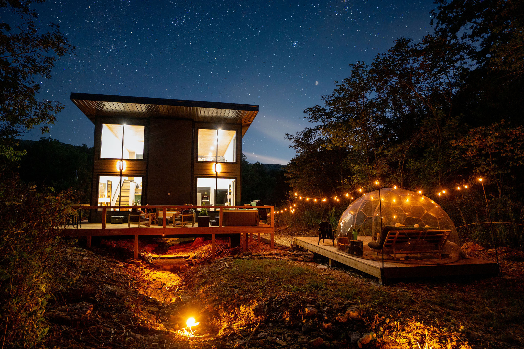 Your private Ozark retreat after dark—glass cabin, stargazing dome and firelight tucked into the woods.