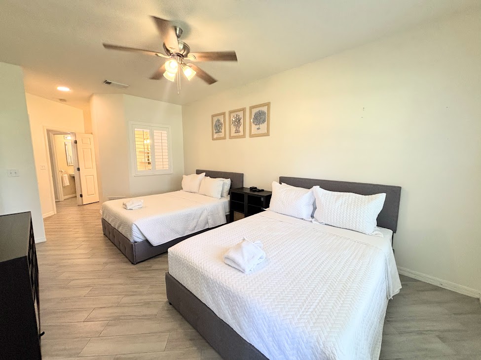 Bright bedroom with two comfortable beds, ceiling fan, modern flooring, and a clean, relaxing setup.