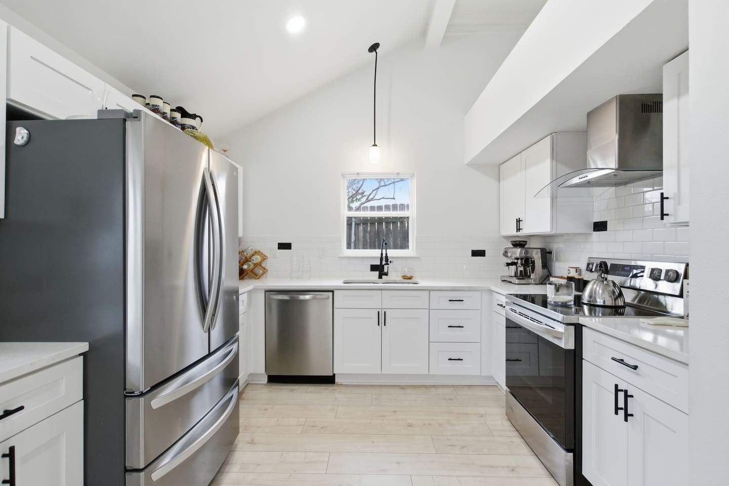Open, modern kitchen featuring full-size fridge, sink with window view, dishwasher, and ample cabinet storage.