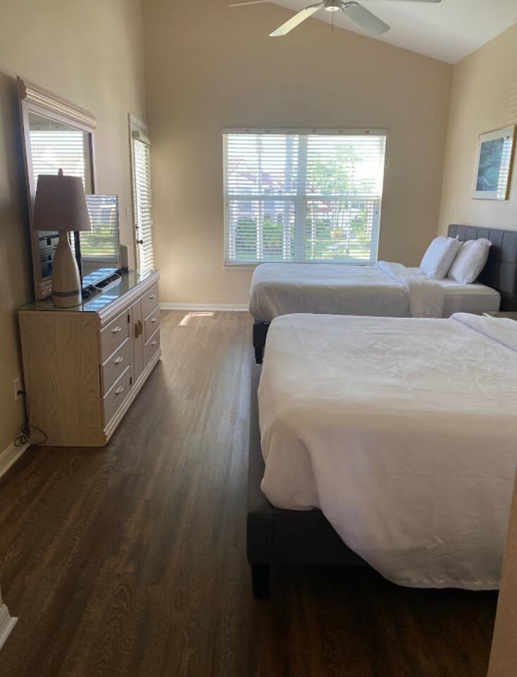 Comfortable bedroom with two beds, dresser storage, TV, wood-look flooring, and natural light.