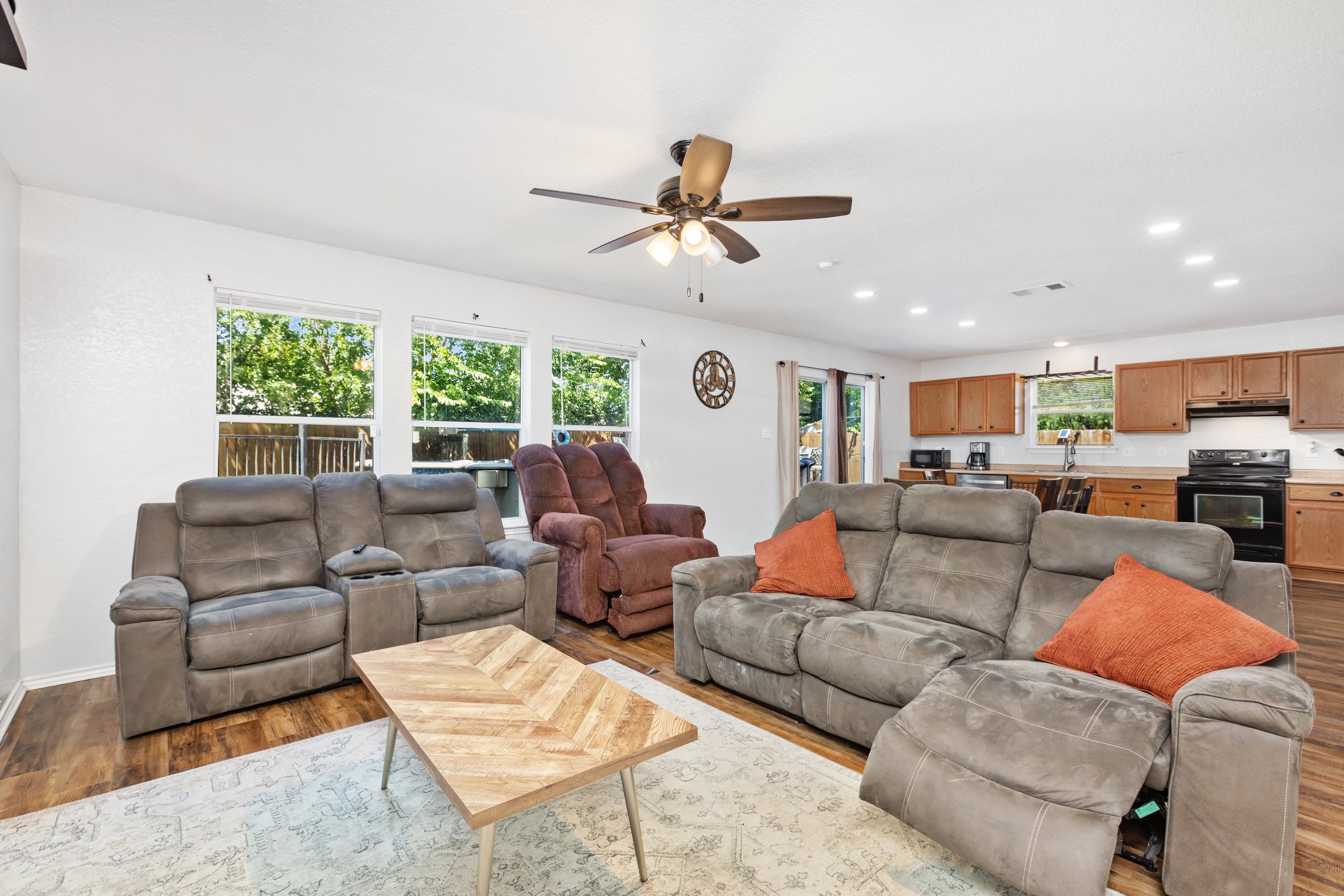 Open-concept living area with reclining sectional, hardwood floors, and ceiling fan. Flows directly into the fully equipped kitchen and dining space — ideal for groups who cook, eat, and relax together.