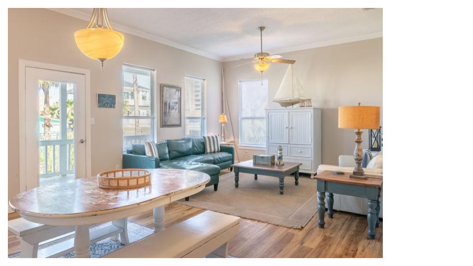 Bright and airy open-concept living space with vaulted ceilings and coastal charm. Relax on plush seating with nautical-inspired accents, enjoy natural light from multiple windows, and take in views of the kitchen and dining areas. 