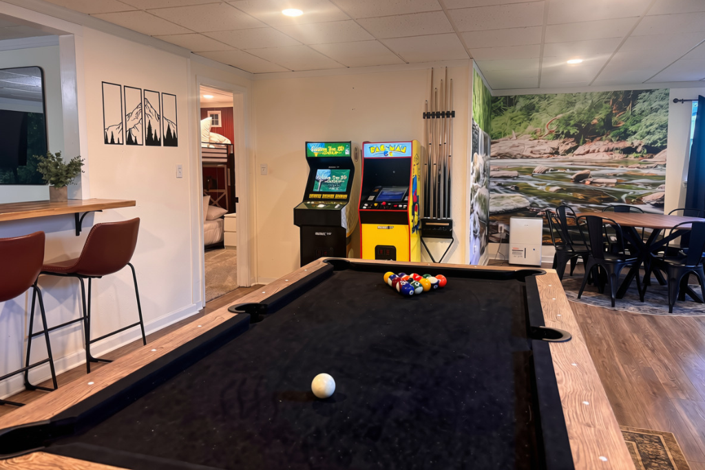 Pool table, two arcade cabinets, bar seating, and a dining spot — the whole lower level is built for the hours between hiking and bed.